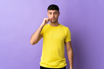 Young Colombian man isolated on purple background showing a sign of silence gesture