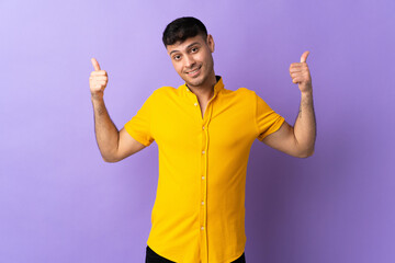 Young Colombian man isolated on purple background giving a thumbs up gesture