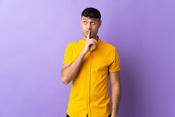 Young Colombian man isolated on purple background showing a sign of silence gesture putting finger...