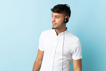 Telemarketer Colombian man working with a headset over isolated background looking to the side and...