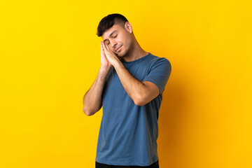 Young Colombian man isolated on yellow background making sleep gesture in dorable expression