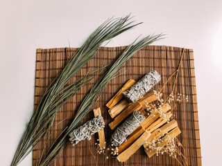 incense on a bamboo brown stand close-up, palo santo from Peru and California white sage, dried flowers around. Art background for text with natural incense and light background blur