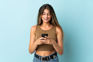 Young caucasian woman isolated on blue background sending a message with the mobile