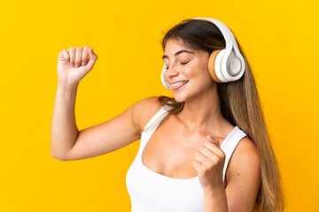 Young caucasian woman isolated on yellow background listening music and dancing