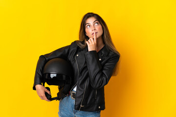 Woman holding a motorcycle helmet isolated on yellow background having doubts while looking up