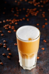 Latte macchiato coffee on a dark background. Glass of latte macchiato and scattered coffee beans. Vertical format