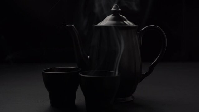 Teiera e tazzine nere con bevanda calda fumante