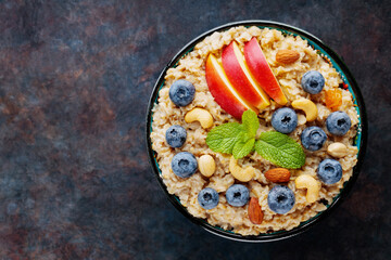 Oatmeal porridge with blueberries, apple slices and nuts. Bowl of oatmeal on dark background. Vegetarian food concept. Healthy food. Copy space. Top view