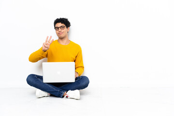 Venezuelan man sitting on the floor with laptop happy and counting three with fingers