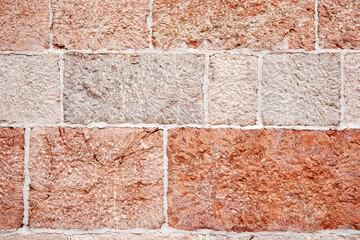 Textured of an old wall with many pink and peach stone tiles. Traditional European architecture.