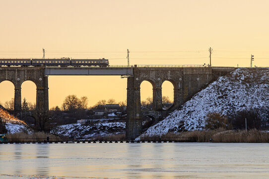 Train passing on a high old bridge over the river, winter river in ice and snow. Stone railway bridge with arches, viaduct in Kropyvnytskyi