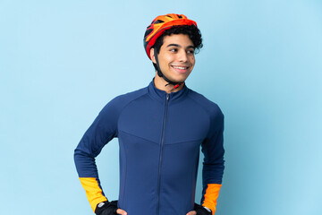 Venezuelan cyclist man isolated on blue background posing with arms at hip and smiling - obrazy, fototapety, plakaty
