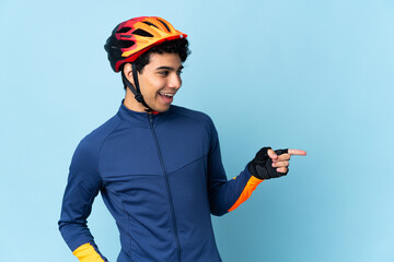 Venezuelan cyclist man isolated on blue background pointing finger to the side and presenting a product - obrazy, fototapety, plakaty