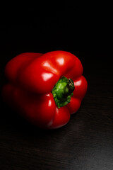 Ripe sweet red pepper lies on a dark background. Vertical photo.