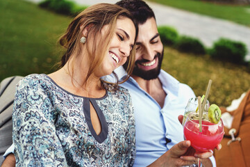 Romantic couple sitting in the luxury resort garden drinking cocktails and joining heads together