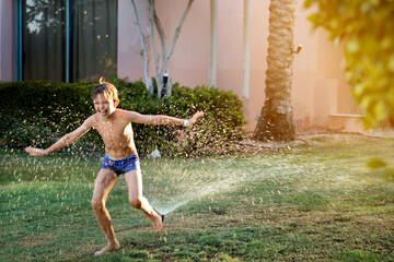 Obraz premium summer. a cheerful boy in the shops jumps under a water fountain