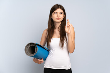 Young Ukrainian sport girl going to yoga classes while holding a mat with fingers crossing and wishing the best