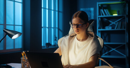 Intelligent caucasian young girl teenager uses computer to watch online school lessons, doing...