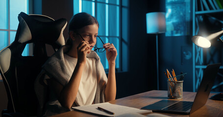 Tired bored smart young teenage girl takes off glasses to rest from study remotely and watching video lesson. Education during pandemic.