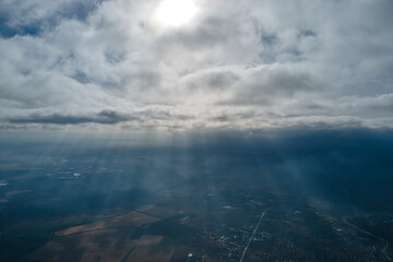 Aerial view from airplane window at high altitude of distant city covered with layer of thin misty smog and distant clouds in evening