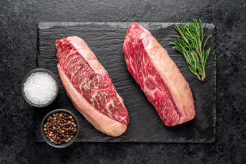 Two raw picanha steaks with spices on a stone background