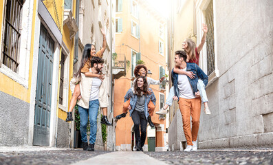 Couples of tourists riding in piggybacking having fun walking on city streets - Group of...