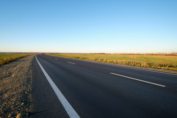 Naklejka premium Empty intercity road with asphalt surface and white markings in evening