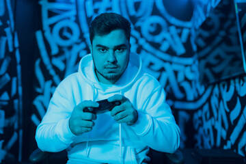 Young man plays on game console with gamepad looking to camera monitor portrait