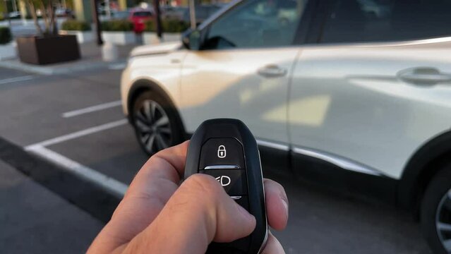 Point of view of male hand opening white suv car with remote key in car park during sunset