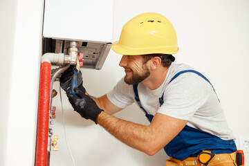 Side view of handyman, technician using screwdriver while fixing boiler or water heater, working on...