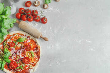 Food background with homemade pizza on grey kitchen table with wooden rolling pin, tomatoes and...
