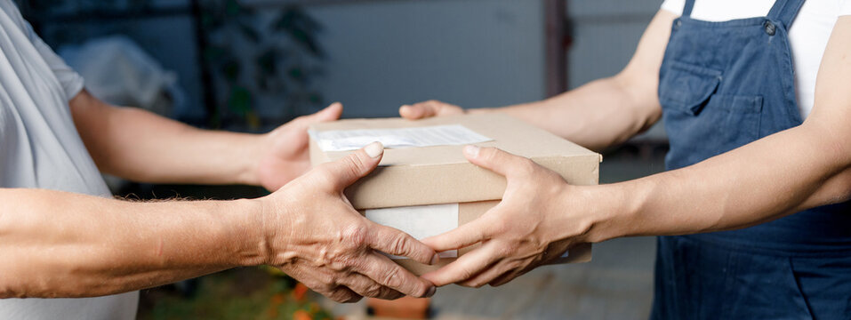 delivery postman handing a parcel box to the recipient, accepting a parcel from a cardboard box from a postal item, the concept of a home courier and a delivery service