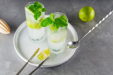 Cocktail mojito and bar accessories on gray background. Two highball glasses of mojito on a white plate. Summer cocktail with lime and mint