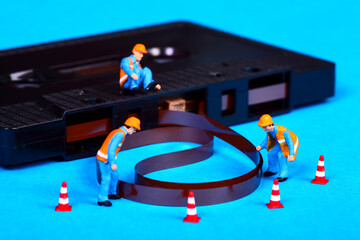 Conceptual image of miniature figure workmen inspecting an old vintage retro cassette tape that has unravelled after a tape jam