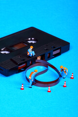 Conceptual image of miniature figure workmen inspecting an old vintage retro cassette tape that has...
