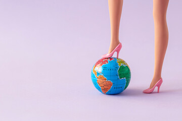 Girl doll legs with high heels and a planet earth against purple background. Creative composition of global domination. Minimal awareness concept