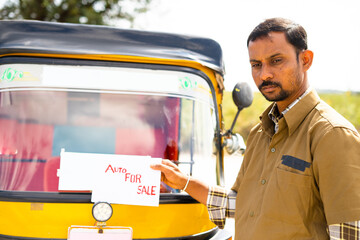 sad auto driver placing auto rikshaw for sale sign board in front of auto - concept of business...