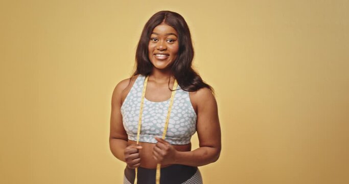 African American woman with long brunette wavy hair wearing sports top shows biceps muscles on shoulders after exercising closeup