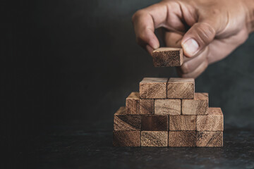 Hand place wooden block stack in pyramid stair step concept of prevent collapse or crash of financial business and risk management or strategic planning and insurance.