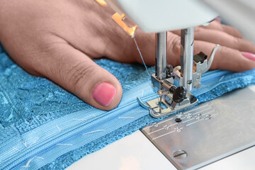 Women's well-groomed hands sew a blue lace dress behind a sewing machine. The process of inserting...