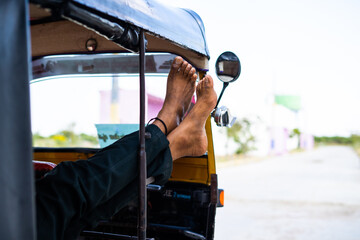tired auto driver sleeping by shaking leg outside tuk-tuk - concept of Taking break, relaxation,...