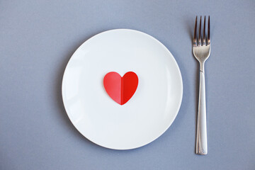 Red Heart on a white plate with fork on grey background