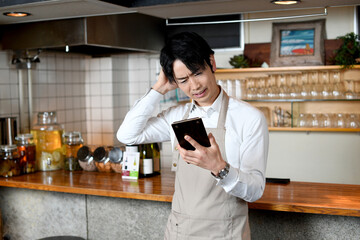 飲食店（レストラン）で悩むエプロン姿のアジア人の男性