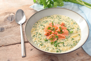 Homemade vegetarian cream soup from parsley leaves and potatoes with strips of smoked salmon on a rustic wooden table, copy space, selected focus