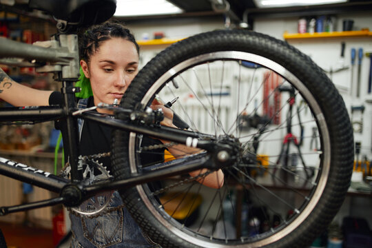 Female Mechanic With Wrench Repairing Bike In Workshop