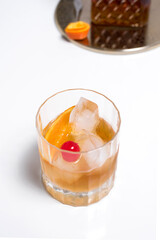 Vaso de vermut con hielo decorado con cerezas y rodajas de naranja sobre mesa blanca	