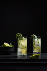 Dos vasos de refrescante cóctel de desintoxicación de jugo de lima con rodajas de lima y hielo sobre fondo negro	