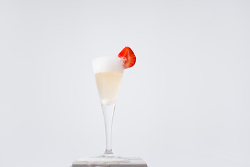 Copa de champán burbujeante derramado adornado con una fresa sobre fondo gris claro. Celebración	