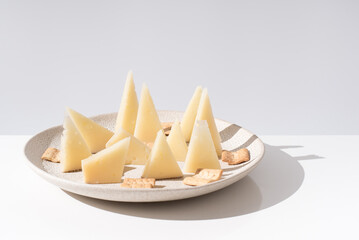 Trozos de queso manchego de oveja curado con tostadas de pan crujiente sobre una mesa blanca. Tapas...