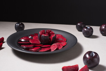 Rodajas de ciruelas negras y ciruelas enteras en un plato negro sobre una mesa gris	